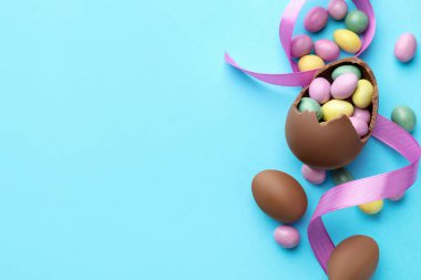 Çikolatalı Paskalya yumurtaları ve açık mavi arka planda menekşe kurdelesi. Metin için boşluk
