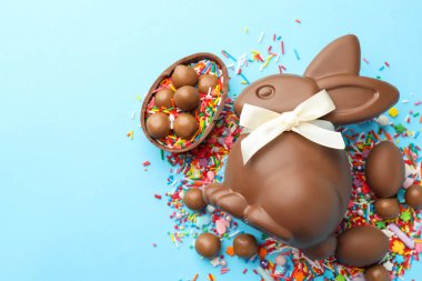 Çikolatalı Paskalya tavşanı, şekerli yumurta ve açık mavi arka planda serpiştirilmiş çikolata, düz yatak. Metin için boşluk