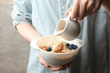 Kadın, arka planda yulaf, fındık ve yaban mersinli kâseye badem sütü döküyor. Yakın plan.