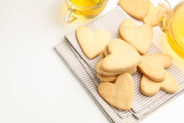 Lezzetli kalp şeklinde tereyağlı kurabiyeler ve beyaz masada çay, yakın plan. Metin için boşluk