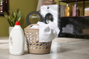 Çamaşır sepetinin içinde giysiler ve yerde deterjan var. Metin için boşluk