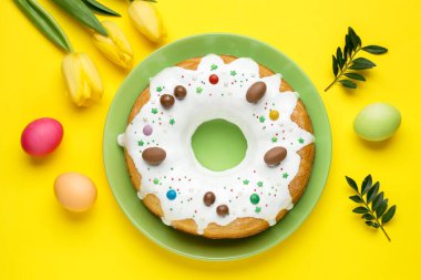 Lezzetli Paskalya pastası, boyanmış yumurtalar, güzel laleler ve sarı arka planda yeşil yapraklar.