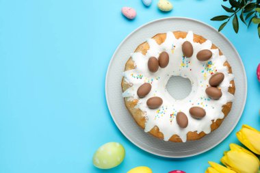 Lezzetli Paskalya pastası, boyanmış yumurtalar, güzel laleler ve açık mavi arka planda yeşil yapraklar. Metin için boşluk