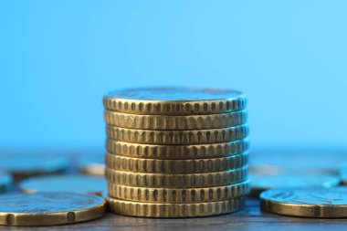 Açık mavi arkaplana karşı ahşap masadaki bozuk paralar yığını, yakın plan