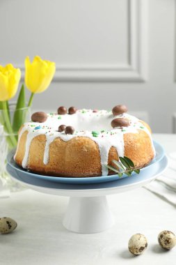 Lezzetli Paskalya pastası, sarı laleler ve bıldırcın yumurtaları beyaz masada, yakın plan.