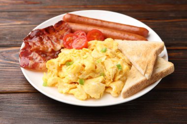 Lezzetli bir kahvaltı. Pastırmalı omlet, sosis, domates ve ahşap masada kızarmış ekmek, yakın plan.