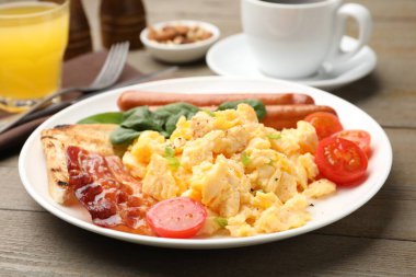 Lezzetli bir kahvaltı. Lezzetli çırpılmış yumurta, domuz pastırması, sosis ve domatesler ahşap masada servis edilir, yakın plan.