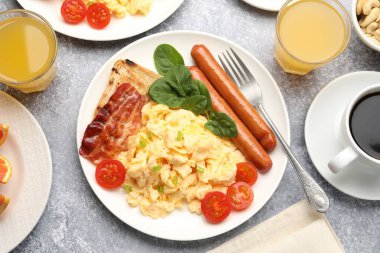 Lezzetli bir kahvaltı. Lezzetli çırpılmış yumurta, domuz pastırması, sosis ve domatesler gri dokuma masasında servis ediliyor.