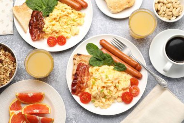 Lezzetli bir kahvaltı. Lezzetli çırpılmış yumurta, domuz pastırması, sosis ve domatesler gri dokuma masasında servis ediliyor.