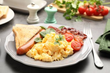 Lezzetli bir kahvaltı. Gri masada servis edilen domuz pastırmalı, sosisli ve domatesli nefis omlet, yakın plan.