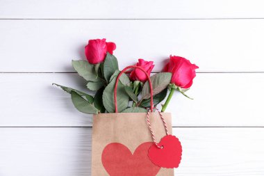 Beyaz ahşap arka planda güller olan hediye çantası, üst manzara. Sevgililer Günü