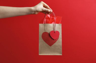 Kırmızı arka planda kalbi olan hediye paketi tutan kadın, yakın plan. Sevgililer Günü