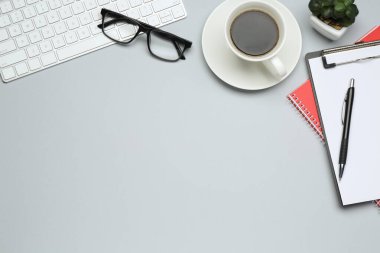 Ofis işyeri. Kırtasiye malzemeleri, kahve, bilgisayar klavyesi, açık gri arka planda gözlük ve çiçek dekoru, düz yatış. Metin için boşluk