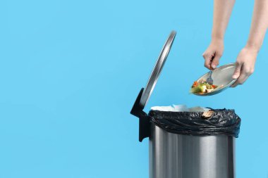 Açık mavi arka planda çöp tenekesine yemek atan bir kadın, yakın plan. Metin için boşluk