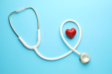 Açık mavi arka planda beyaz steteskop ve kalp modeli. Metin için boşluk