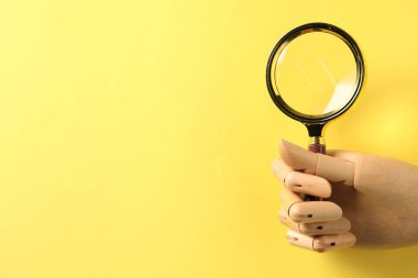 Sarı arka planda büyüteç olan manken eli, yakın plan. Metin için boşluk