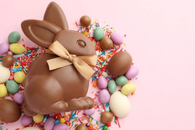 Çikolatalı Paskalya tavşanı, yumurtalar, şekerler ve pembe arka plana serpiştirilmiş şekerler, düz yatak. Metin için boşluk