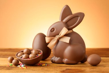 Çikolatalı Paskalya tavşanı, şekerli yumurtalar ve ahşap masa üzerine serpiştirilmiş bej renkli arka plan, yakın plan