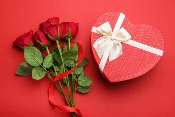 Güzel kalp şeklinde hediye kutusu ve kırmızı arka planda güller, düz yatış. Sevgililer Günü