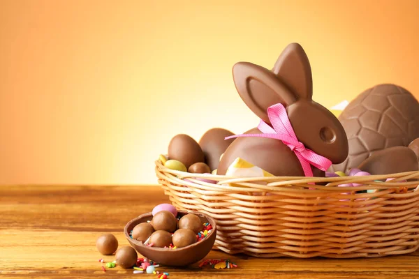 Hasır sepetin içinde yumurta ve şekerlemeli çikolatalı Paskalya tavşanı bej renkli arka planda, yakın plan. Metin için boşluk