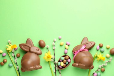 Çikolatalı Paskalya tavşanları, söğüt dalları ve açık yeşil arka planda yumurtalar, düz yatak. Metin için boşluk