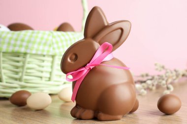 Çikolatalı Paskalya tavşanı ve hasır sepetteki yumurtalar ahşap masada pembe arka planda, yakın plan.