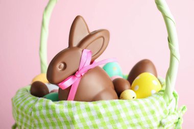 Çikolatalı Paskalya tavşanı ve hasır sepette pembe arka planda yumurtalar, yakın plan.