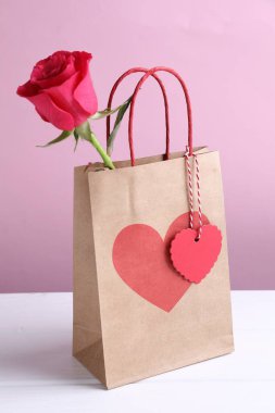 Kalpli hediye çantası ve pembe arka planda beyaz masada gül. Sevgililer Günü