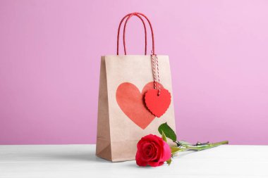 Kalpli hediye çantası ve pembe arka planda beyaz masada gül. Sevgililer Günü