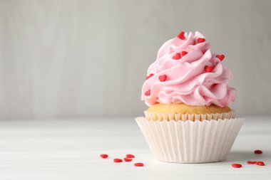 Sevgililer Günün kutlu olsun. Gri duvarın yanındaki beyaz ahşap masada kalp şeklinde serpiştirilmiş lezzetli kek, yakın plan. Metin için boşluk