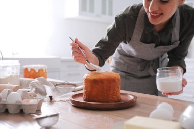 Genç bir kadın geleneksel paskalya pastasını mutfakta jöleli dekore ediyor.