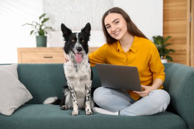 Evdeki kanepede dizüstü bilgisayarı ve sevimli köpeğiyle gülümseyen kadın.
