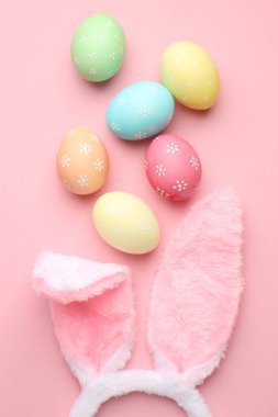 Tavşan kulaklı şirin saç bandı ve pembe arka planda Paskalya yumurtaları, düz yatış.