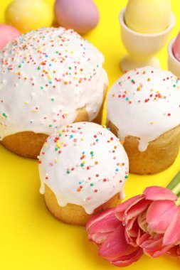 Lezzetli Paskalya pastaları, yumurta ve laleler sarı arka planda, yakın plan.