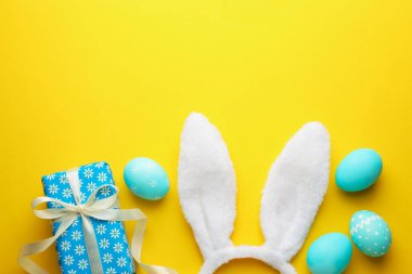 Boyalı Paskalya yumurtaları, tavşan kulaklığı ve sarı arka planda hediye, düz yatak. Metin için boşluk