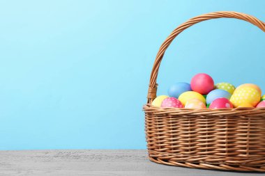Hasır sepetin içine boyanmış Paskalya yumurtaları açık mavi arka planda gri ahşap masa üzerinde. Metin için boşluk