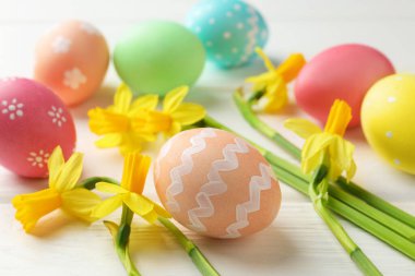 Boyalı Paskalya yumurtaları ve beyaz ahşap masaya güzel nergisler, yakın plan.