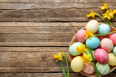 Hasır sepete boyanmış Paskalya yumurtaları ve ahşap masaya serilmiş güzel nergisler. Metin için boşluk