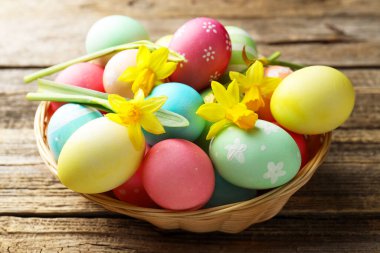 Boyanmış Paskalya yumurtaları ve ahşap masadaki hasır sepetin içindeki güzel nergisler.