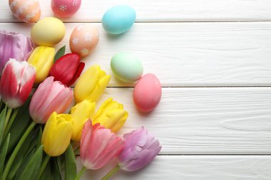 Boyanmış Paskalya yumurtaları ve beyaz ahşap masa üzerinde güzel laleler. Metin için boşluk
