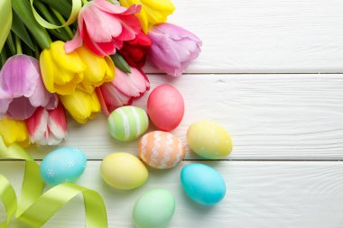 Boyalı Paskalya yumurtaları, güzel laleler ve beyaz ahşap masa şeritleri, düz bir döşeme. Metin için boşluk
