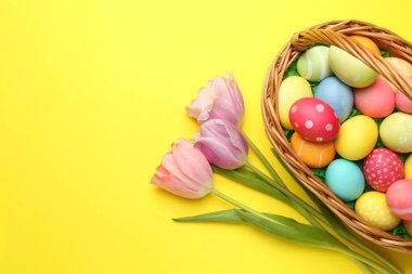 Sarı arka planda boyanmış yumurta ve lalelerin olduğu Paskalya sepeti, düz. Metin için boşluk