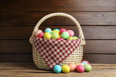 Ahşap masada hasır sepete boyanmış Paskalya yumurtaları.