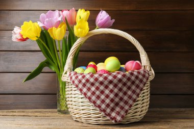Hasır sepete boyanmış Paskalya yumurtaları ve ahşap masada güzel laleler.