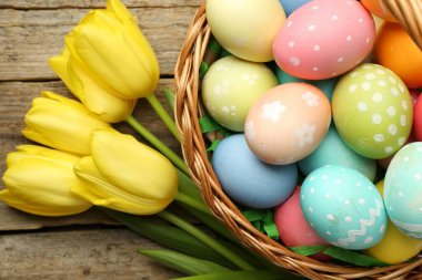 Tahta masanın üzerinde boyanmış yumurtalar ve laleler olan Paskalya sepeti, düz yatıyordu.