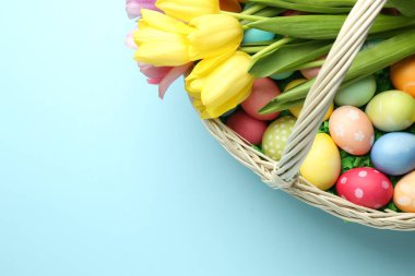 Açık mavi zemin üzerinde boyanmış yumurta ve laleler olan Paskalya sepeti, üst manzara. Metin için boşluk