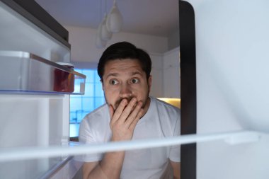 Adam mutfaktaki açık buzdolabına bakıyor, içeriden bakıyor.
