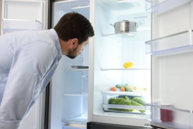 Adam mutfaktaki açık buzdolabına bakıyor.