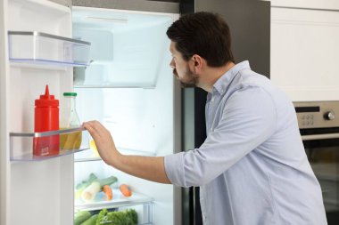 Adam mutfaktaki açık buzdolabına bakıyor.