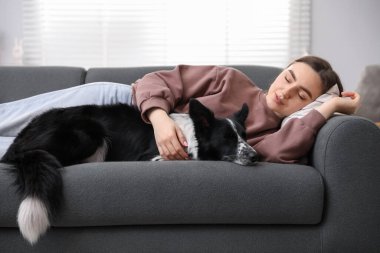 Evdeki kanepede uyuyan sevimli köpeğiyle genç bir kadın.